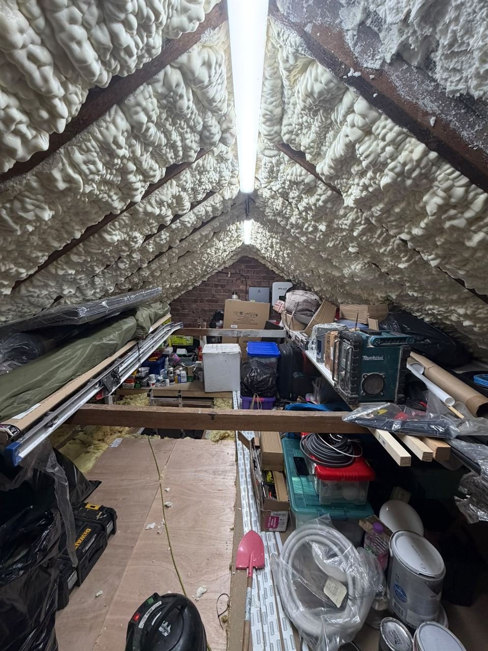 Loft roof with spray foam insulation covering the underside of the roof between the rafters, before it was removed, with a strip light at the ridge