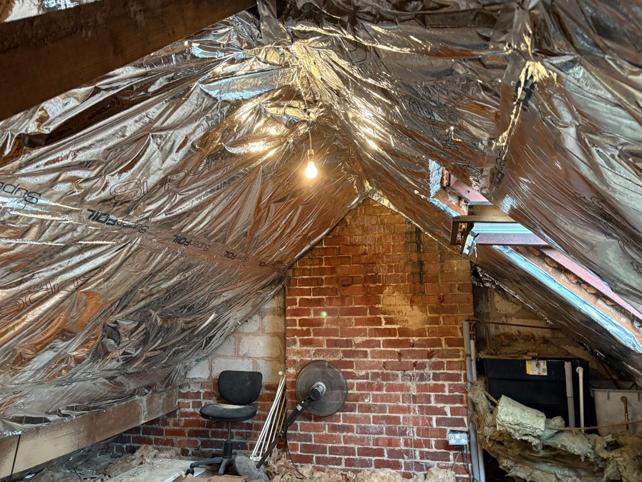Loft roof lined with SuperFOIL insulation, with a brick gable wall and a bare bulb hanging from the ridge