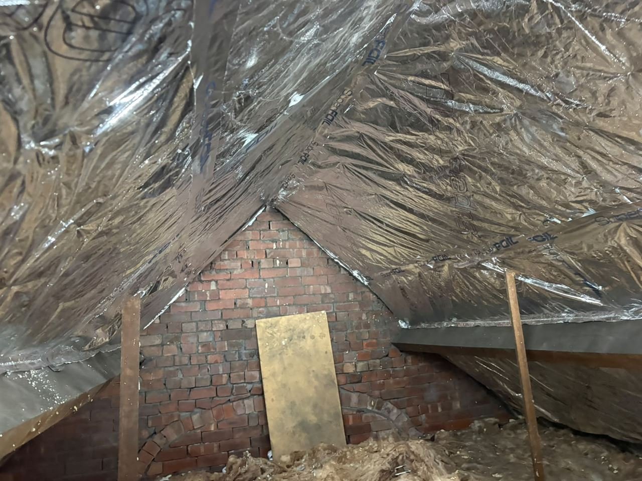 SuperFOIL insulation fitted across the roof slopes of a loft, with the SuperFOIL printing visible and a brick gable end